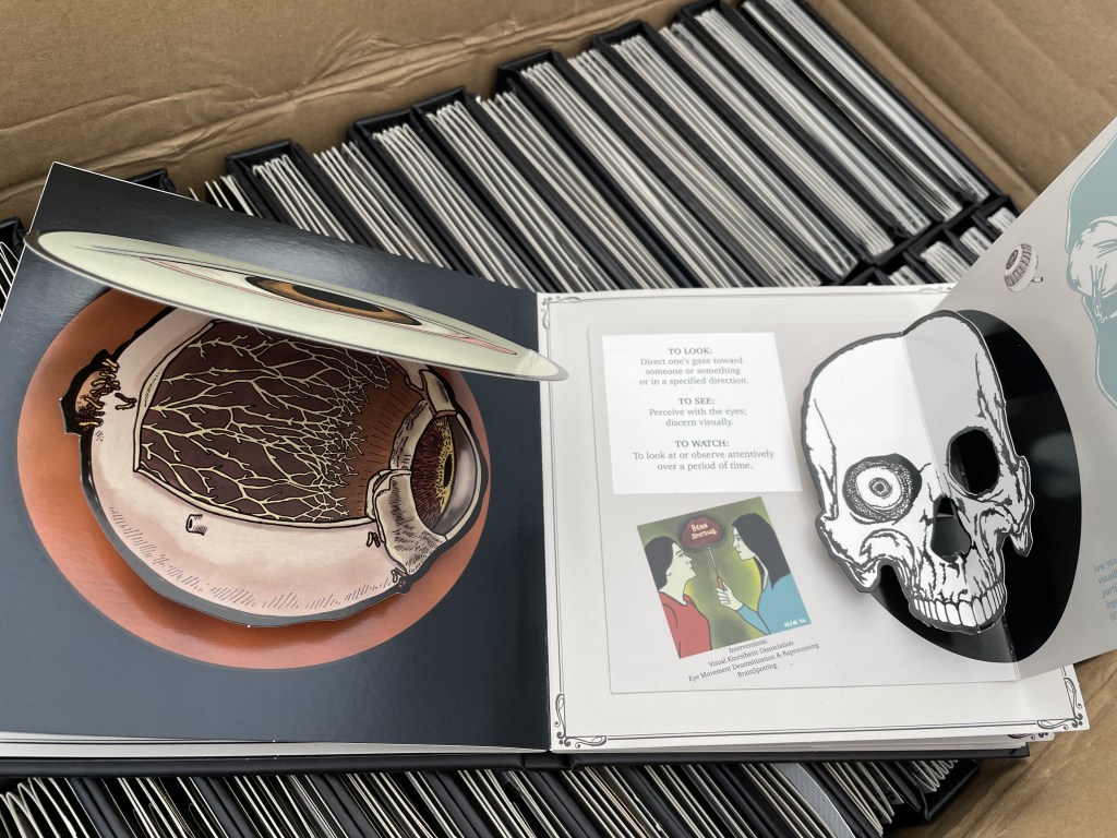 An open spread of a pop-up book depicting the inside of the hua eye as well as a skull with an open eye socket